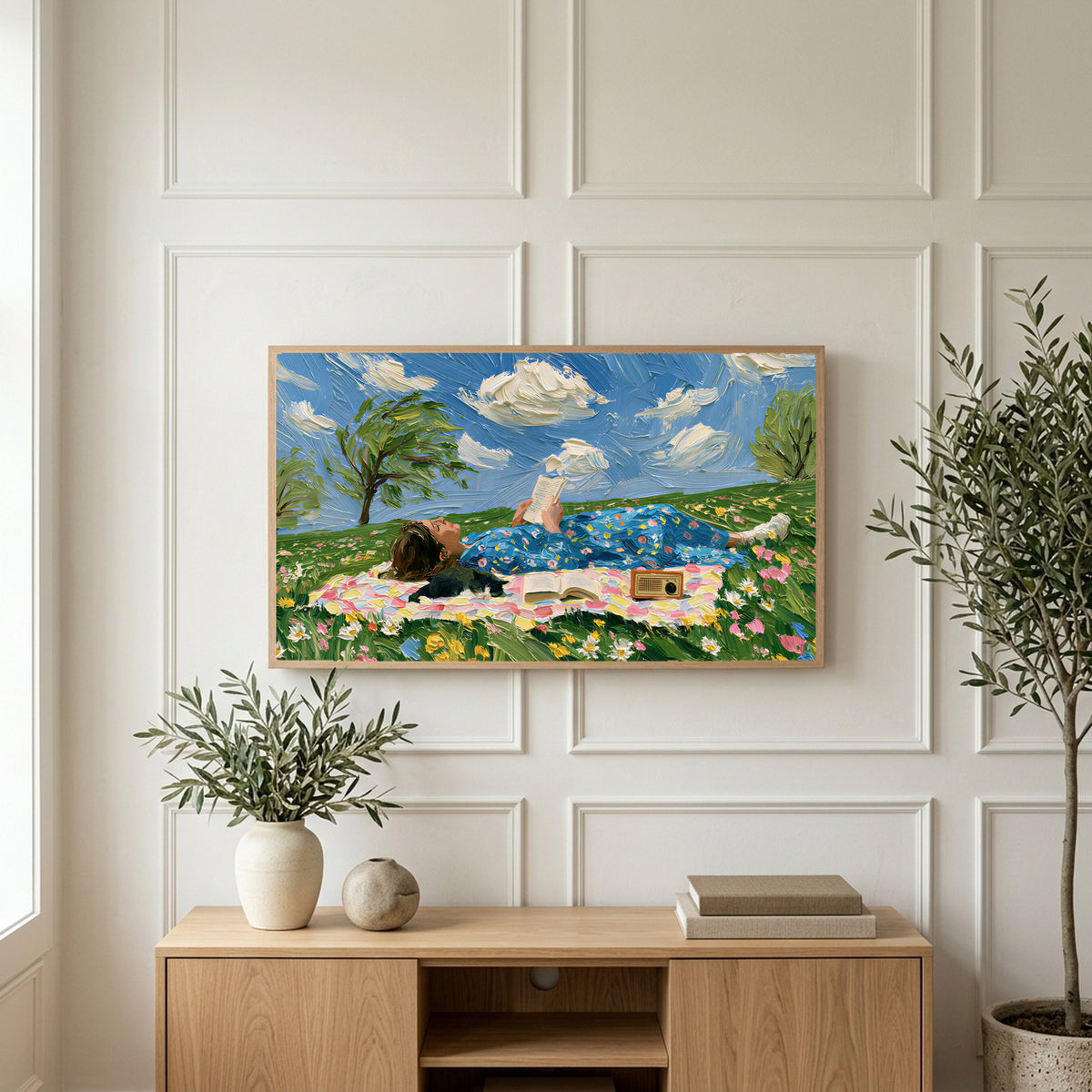 Picnic reader in a meadow art on a TV above a light oak sideboard with olive branches in a bright living room