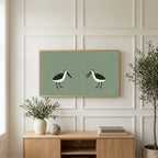 Two shorebirds art on a TV above a light oak sideboard with olive branches in a bright living room
