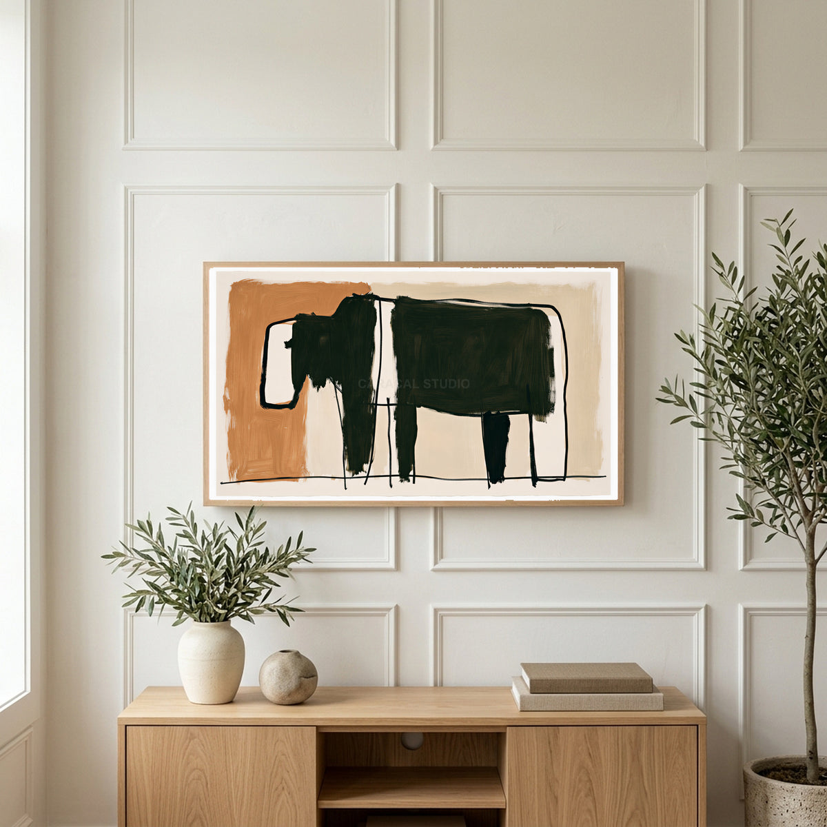 Minimalist black cow art on a TV above a light oak sideboard with olive branches in a bright living room