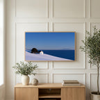 Snowy seaside cottage art on a TV above a light oak sideboard with olive branches in a bright living room