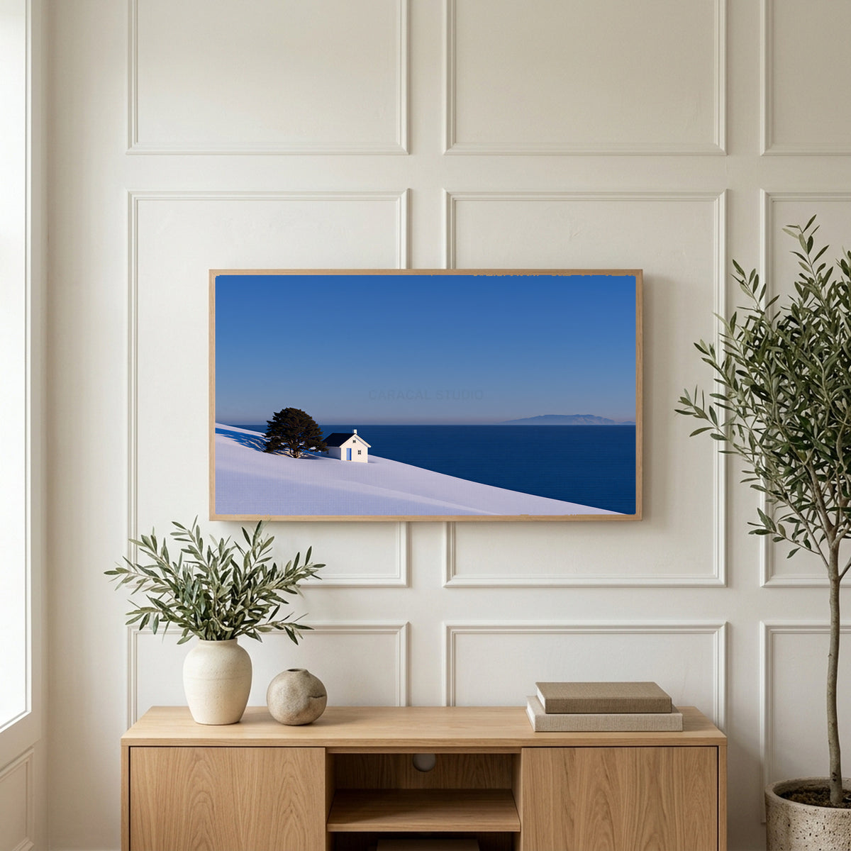 Snowy seaside cottage art on a TV above a light oak sideboard with olive branches in a bright living room