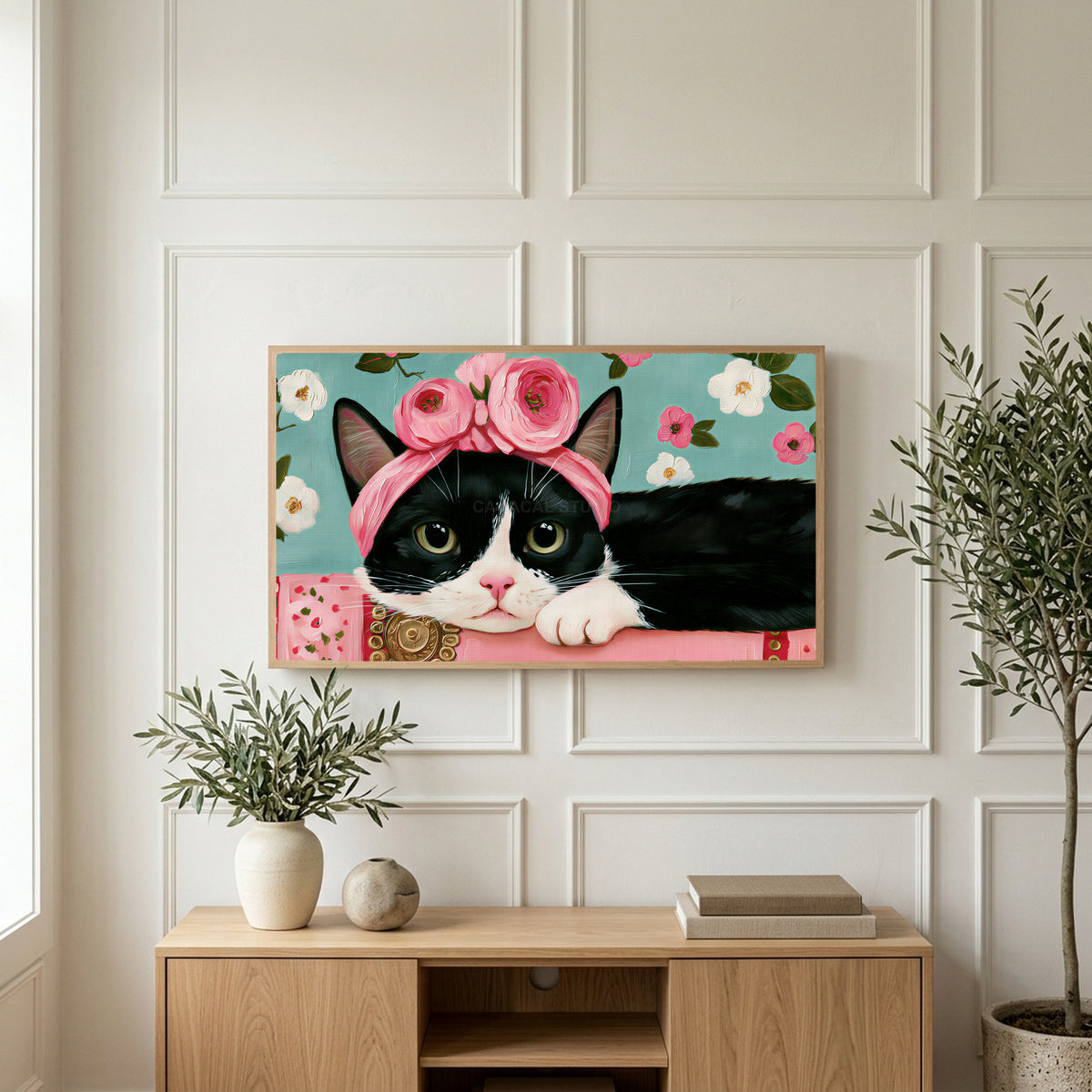 Cat with a flower crown art on a TV above a light oak sideboard with olive branches in a bright living room