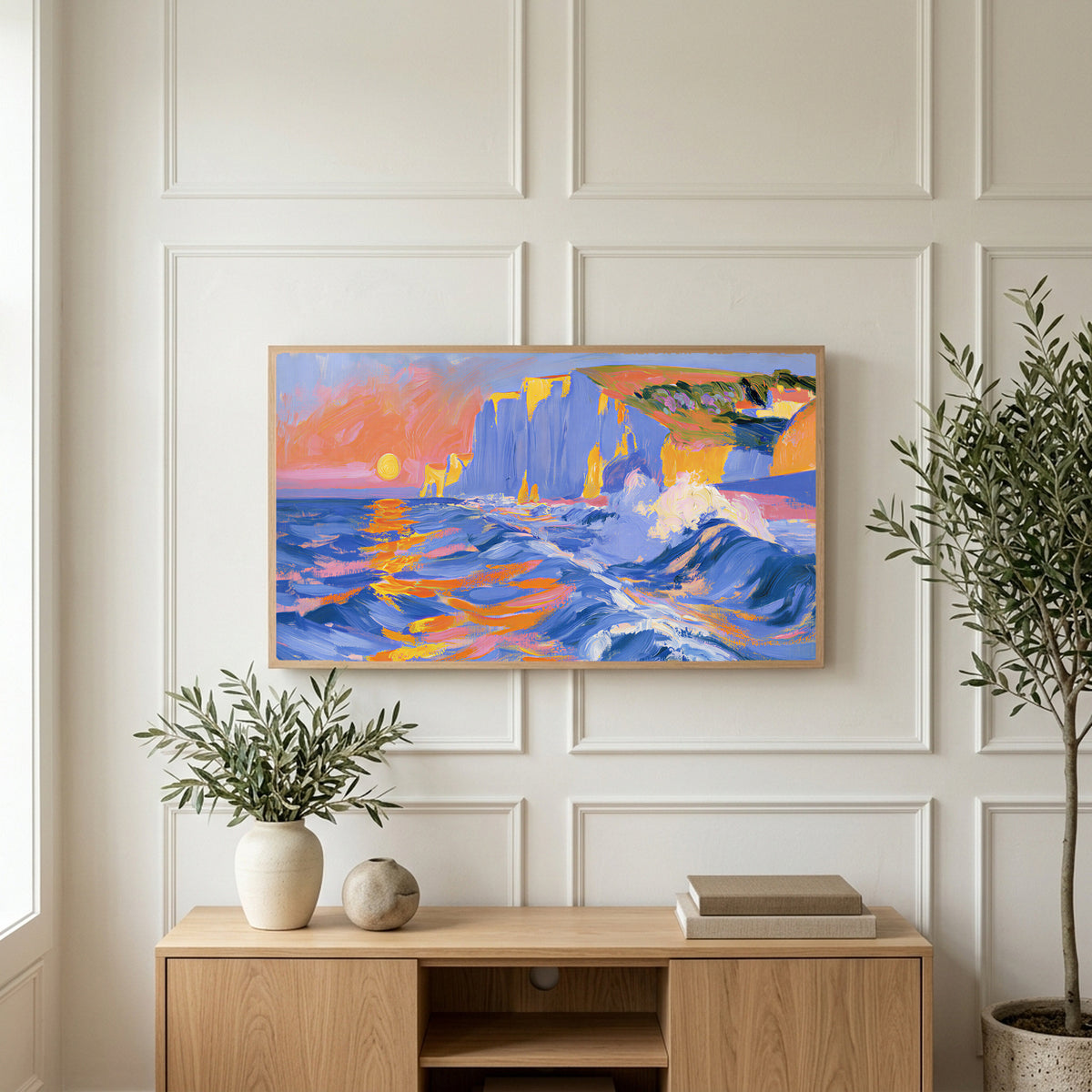 Sunset sea cliffs art on a TV above a light oak sideboard with olive branches in a bright living room