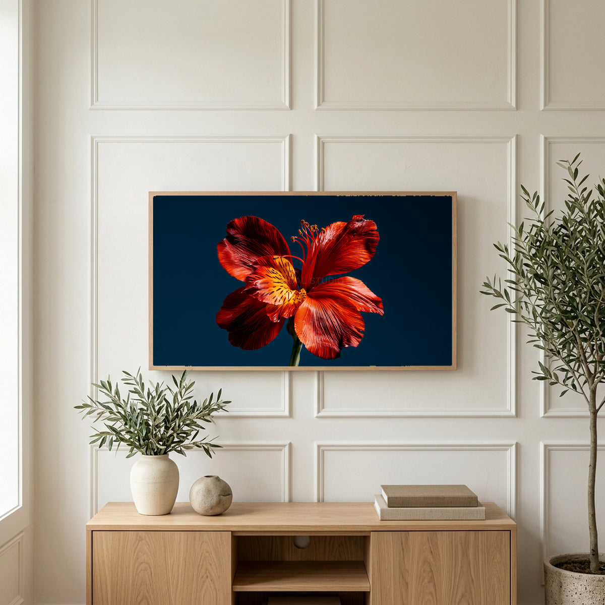 Red lily on navy art on a TV above a light oak sideboard with olive branches in a bright living room
