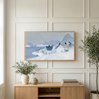 Snowy seaside village art on a TV above a light oak sideboard with olive branches in a bright living room