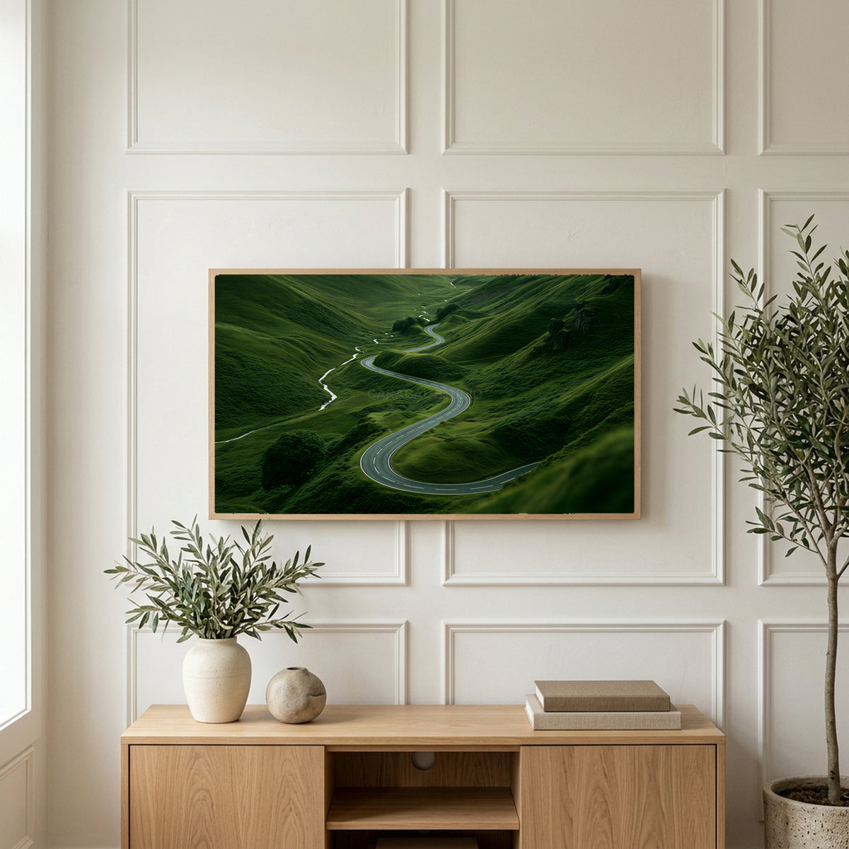 Winding road landscape art on a TV above a light oak sideboard with olive branches in a bright living room