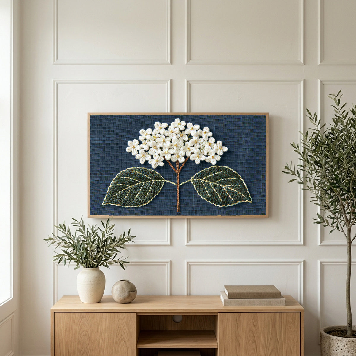 Embroidered hydrangea art on a TV above a light oak sideboard with olive branches in a bright living room