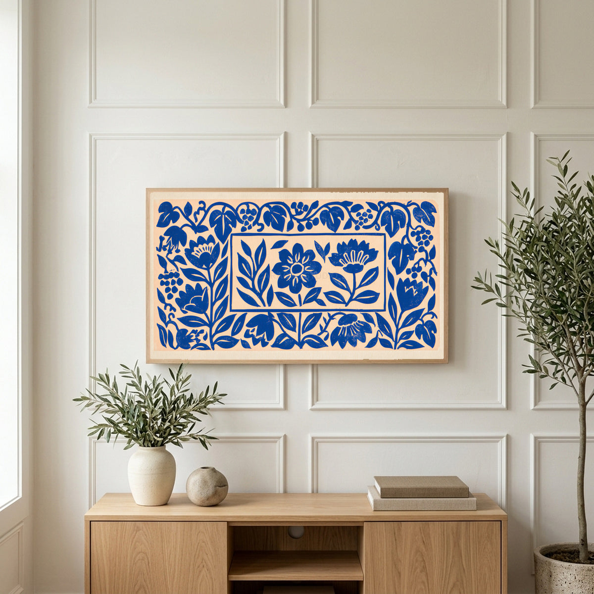 Blue paper cut flowers art on a TV above a light oak sideboard with olive branches in a bright living room