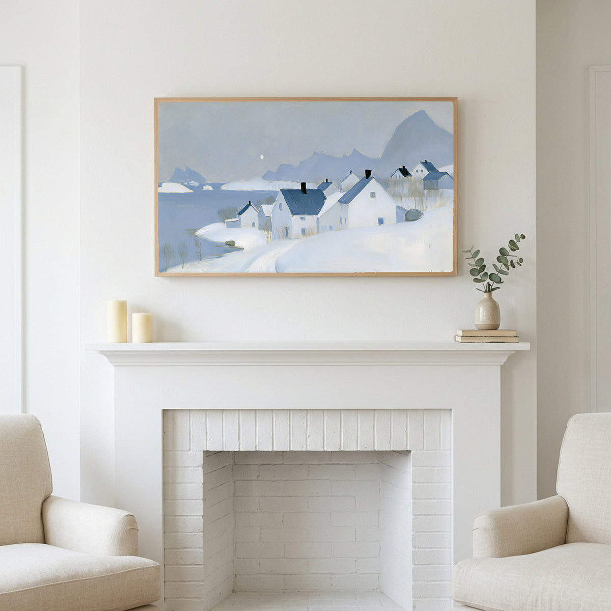 Snowy seaside village art above a white fireplace with candles and eucalyptus on the mantel