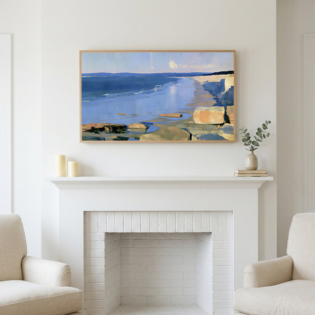 Low tide beach and cliffs art above a white fireplace with candles and eucalyptus on the mantel