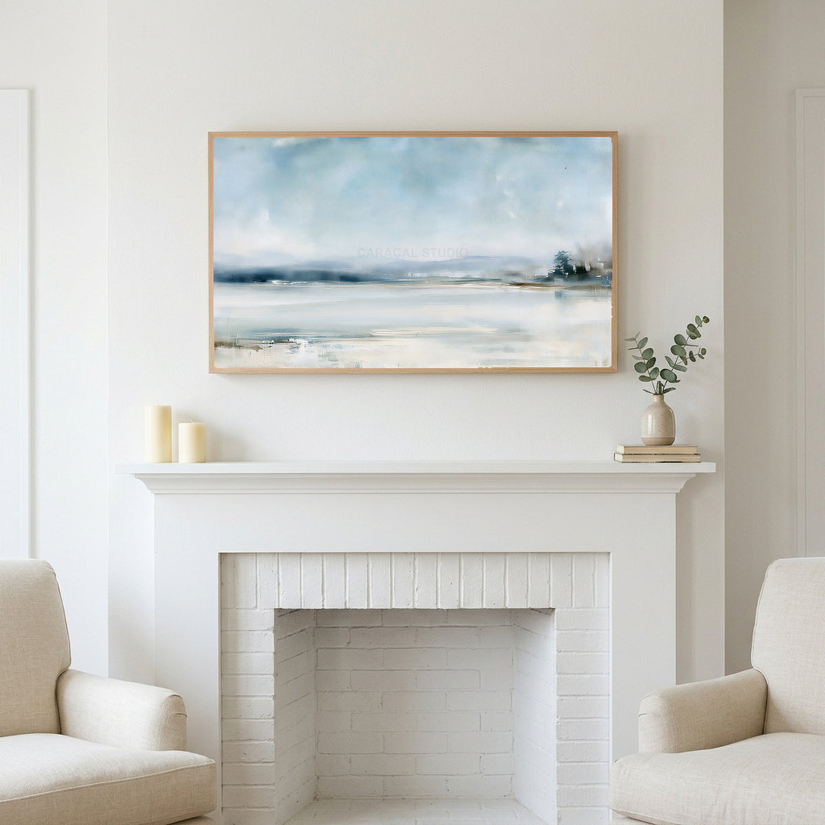 Snowy landscape art above a white fireplace with candles and eucalyptus on the mantel