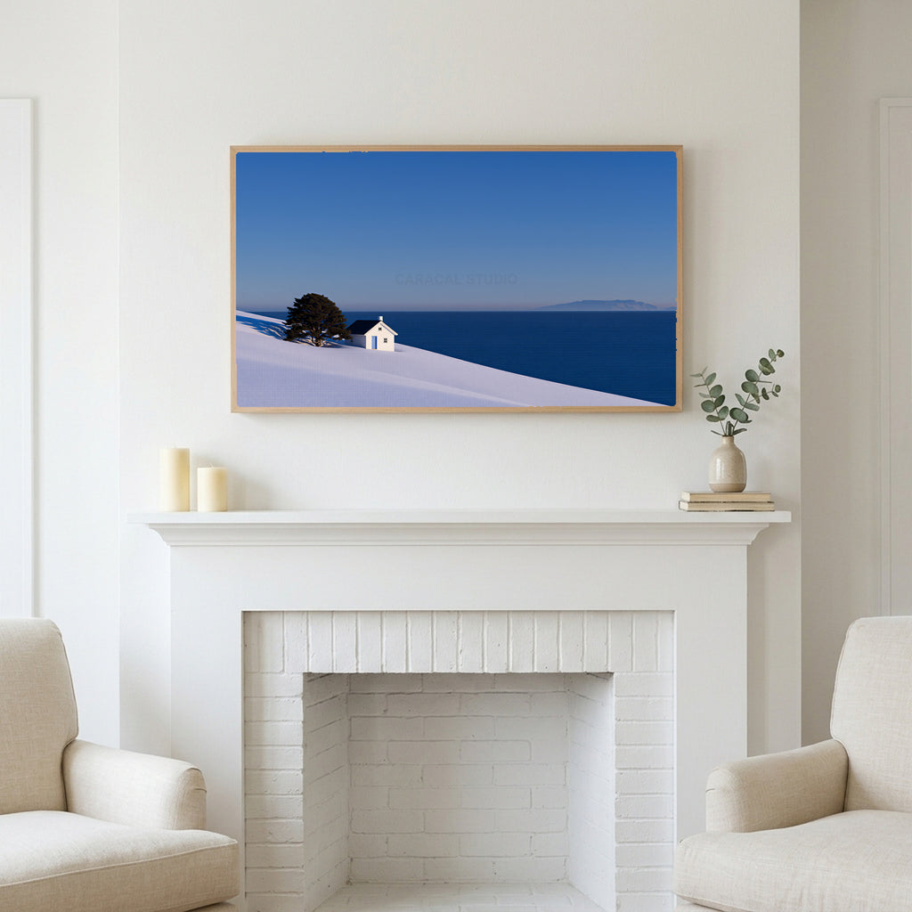 Snowy seaside cottage art above a white fireplace with candles and eucalyptus on the mantel