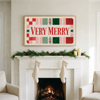 Very Merry typography art on a TV above a white fireplace with a pine garland and cream stockings