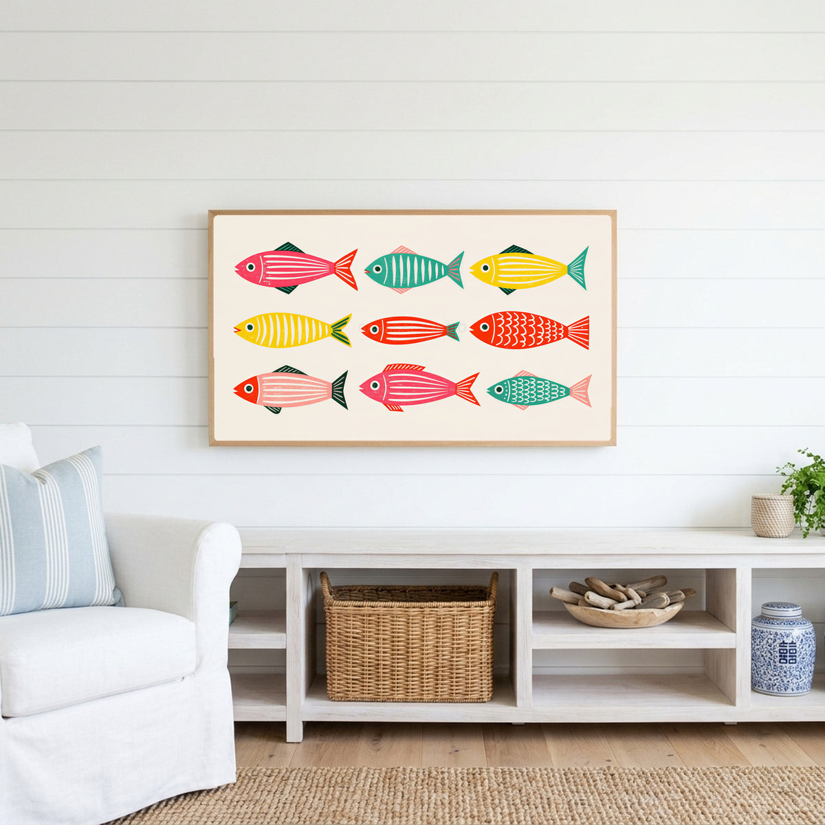 Folk fish Frame TV art above a white console with a rattan basket in a coastal living room