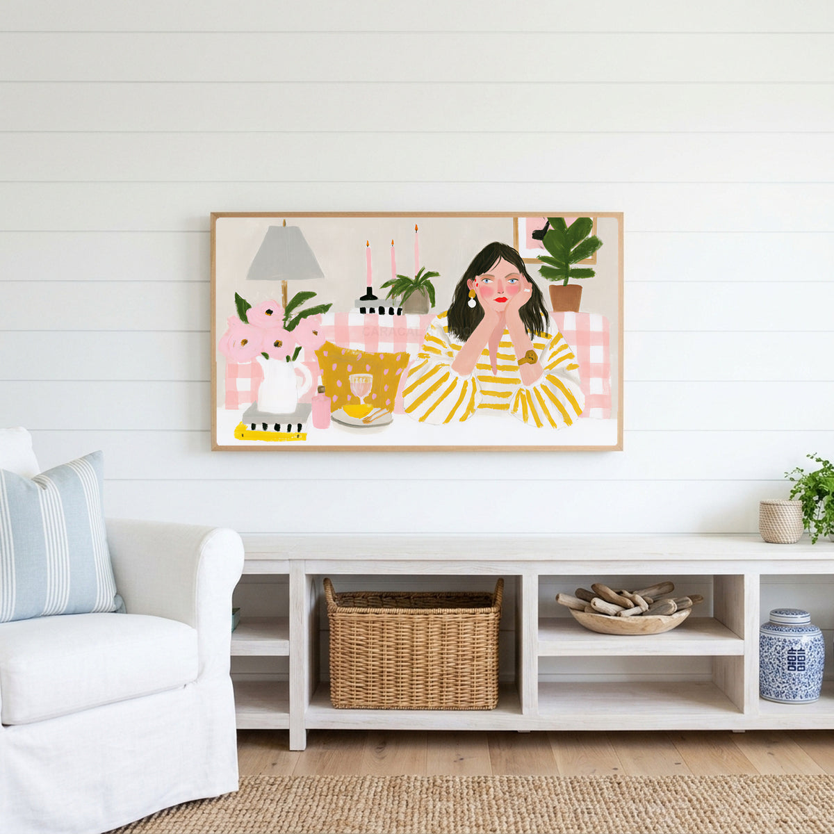 Woman at a pink table Frame TV art above a white console with a rattan basket in a coastal living room