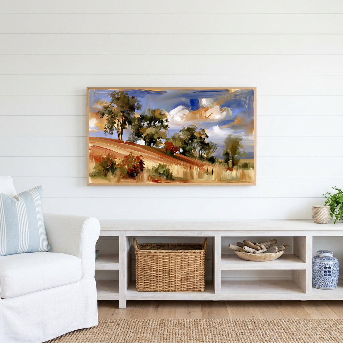 Hillside trees Frame TV art above a white console with a rattan basket in a coastal living room