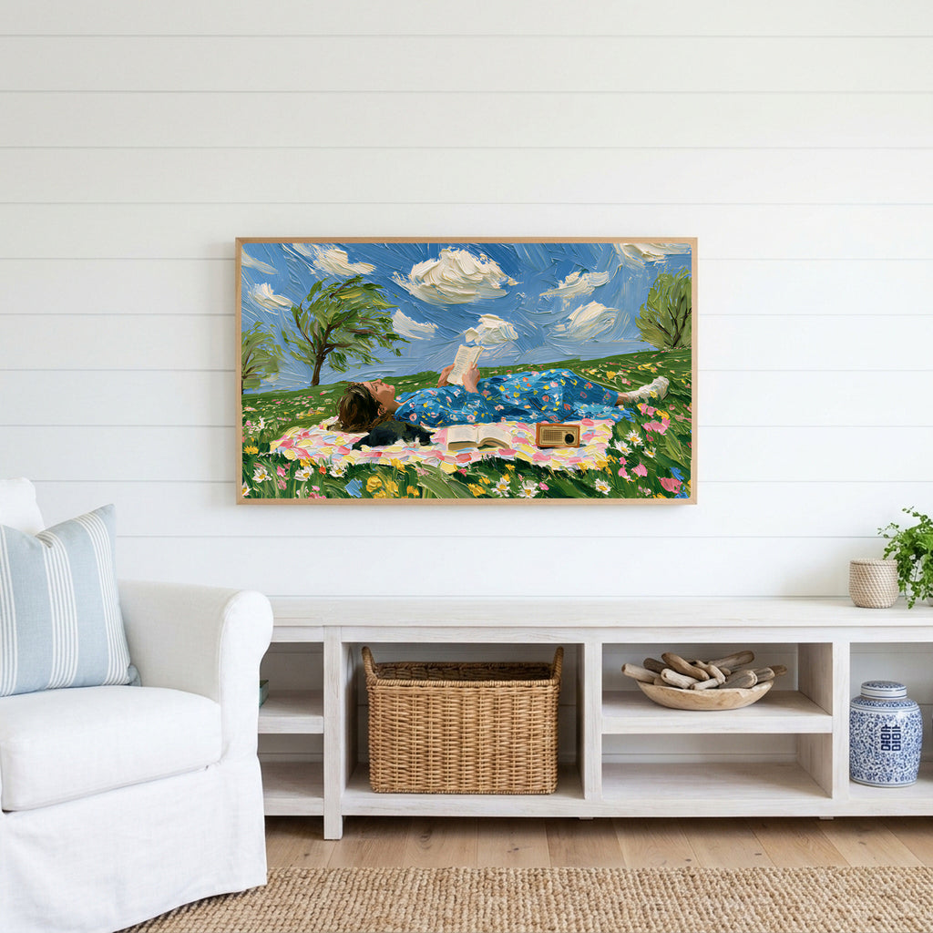 Picnic reader in a meadow Frame TV art above a white console with a rattan basket in a coastal living room