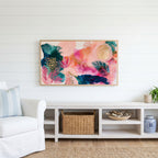 Tropical abstract Frame TV art above a white console with a rattan basket in a coastal living room