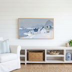 Snowy seaside village Frame TV art above a white console with a rattan basket in a coastal living room