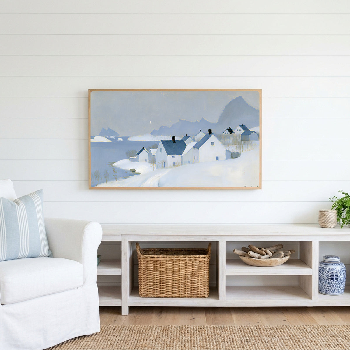 Snowy seaside village Frame TV art above a white console with a rattan basket in a coastal living room