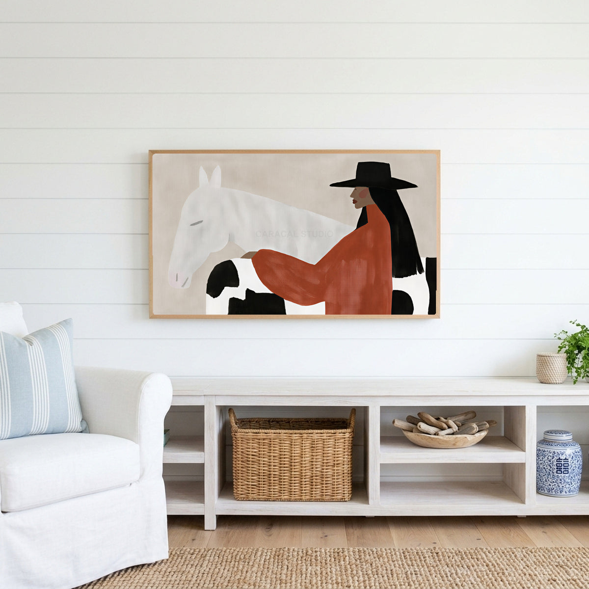 Cowgirl and her horse Frame TV art above a white console with a rattan basket in a coastal living room
