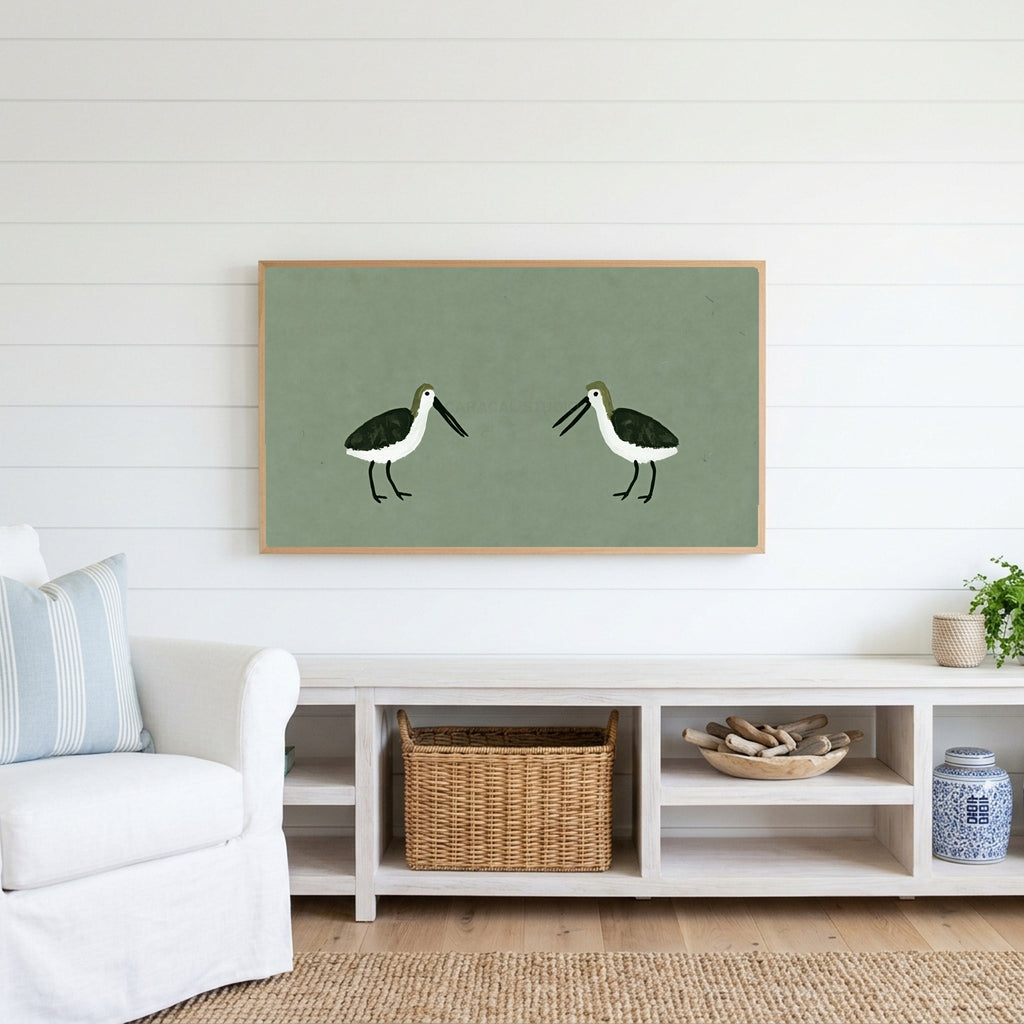 Two shorebirds Frame TV art above a white console with a rattan basket in a coastal living room