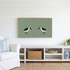 Two shorebirds Frame TV art above a white console with a rattan basket in a coastal living room