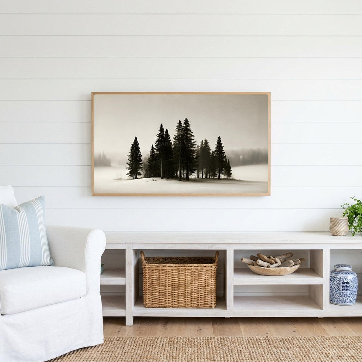 Snowy pine trees Frame TV art above a white console with a rattan basket in a coastal living room