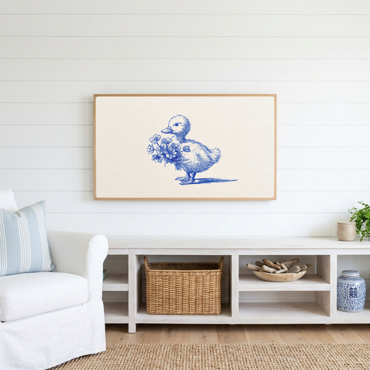Duckling Frame TV art above a white console with a rattan basket in a coastal living room