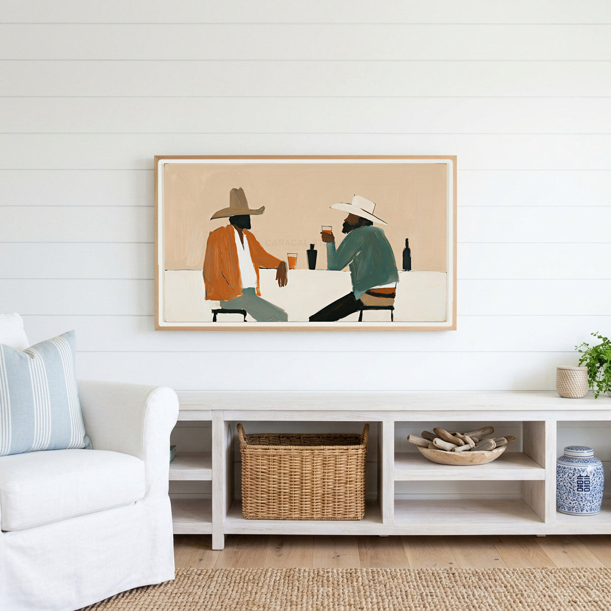 Cowboys and saloon drinks Frame TV art above a white console with a rattan basket in a coastal living room