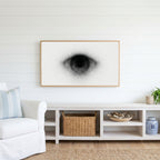 Black and white eye Frame TV art above a white console with a rattan basket in a coastal living room