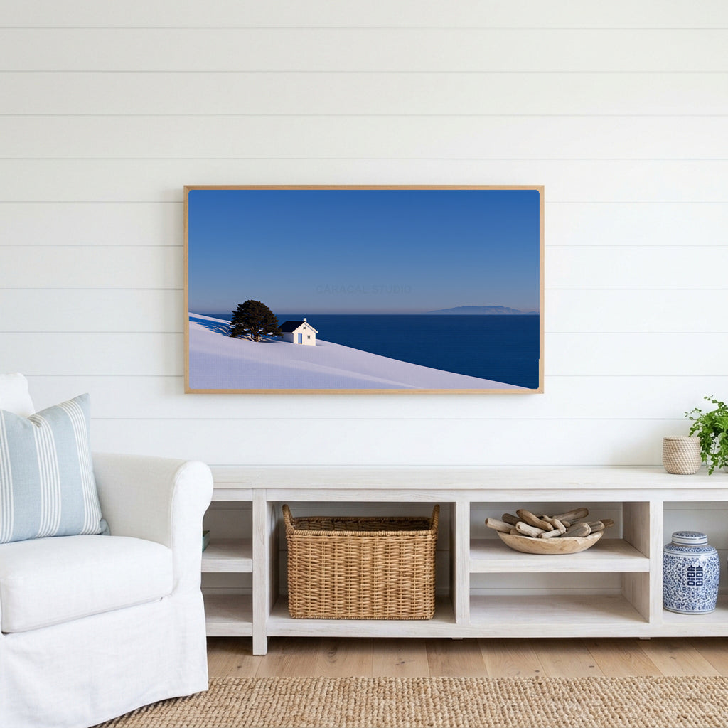 Snowy seaside cottage Frame TV art above a white console with a rattan basket in a coastal living room
