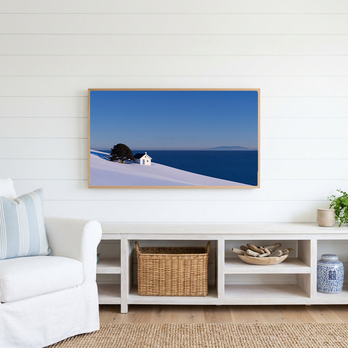 Snowy seaside cottage Frame TV art above a white console with a rattan basket in a coastal living room