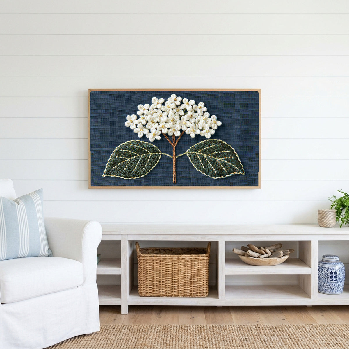 Embroidered hydrangea Frame TV art above a white console with a rattan basket in a coastal living room