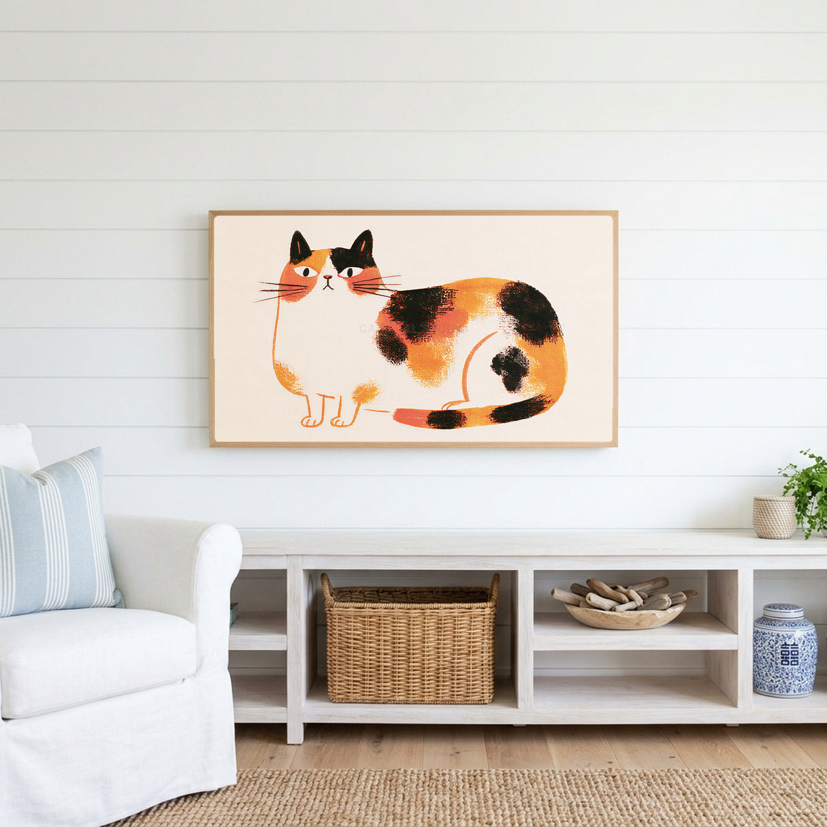 Calico cat Frame TV art above a white console with a rattan basket in a coastal living room