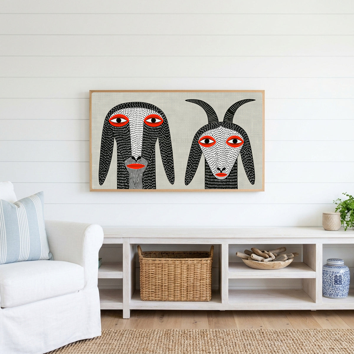 Folk art goats Frame TV art above a white console with a rattan basket in a coastal living room