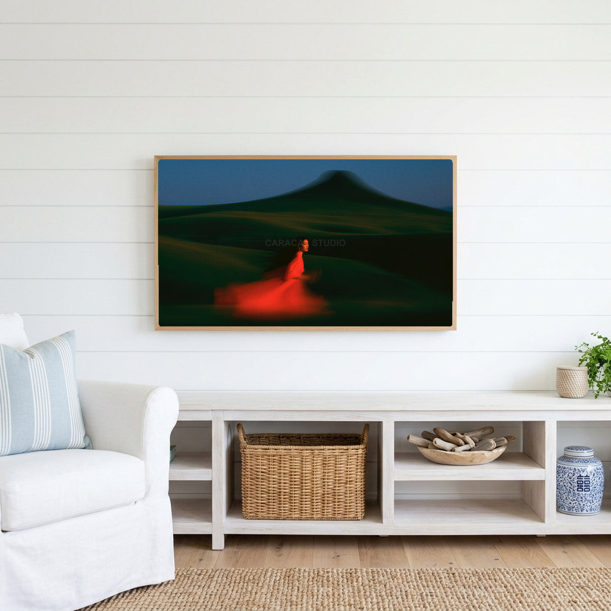 Woman running over green hills Frame TV art above a white console with a rattan basket in a coastal living room