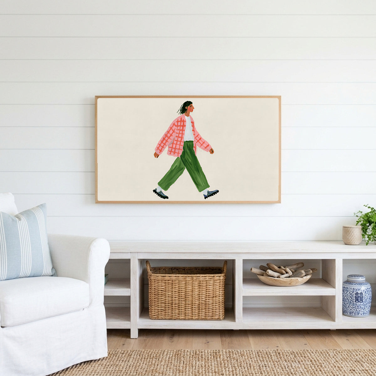 Woman walking Frame TV art above a white console with a rattan basket in a coastal living room