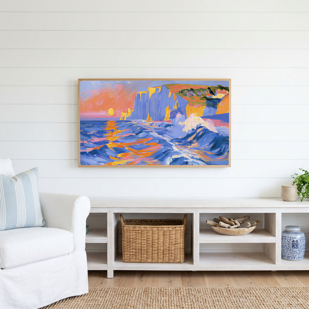 Sunset sea cliffs Frame TV art above a white console with a rattan basket in a coastal living room