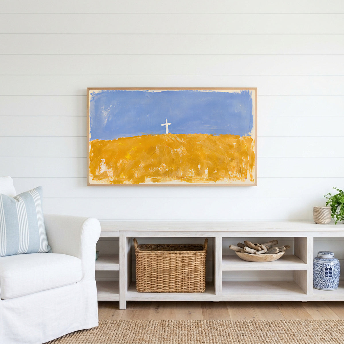 Cross on a golden field Frame TV art above a white console with a rattan basket in a coastal living room