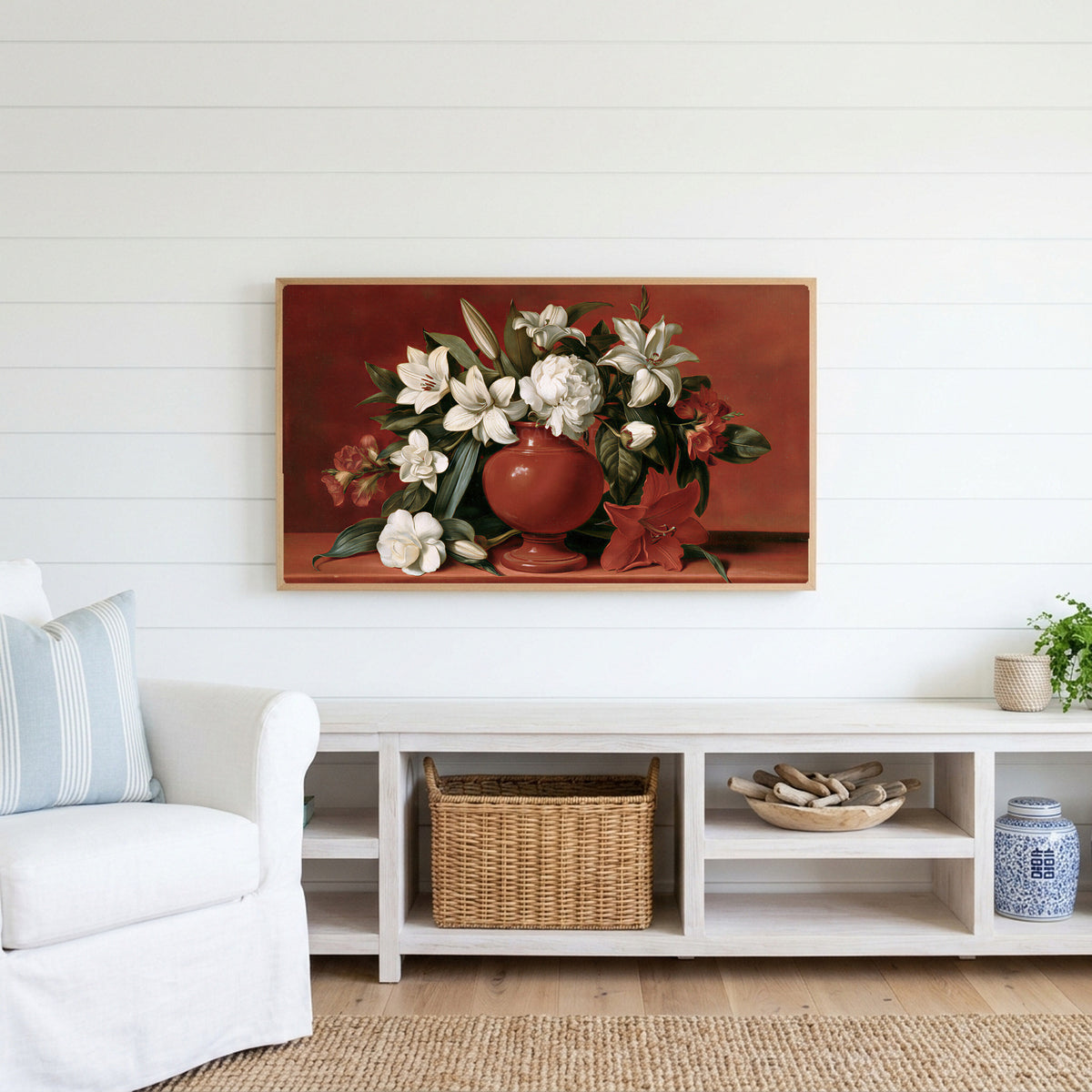 White lilies in a red vase Frame TV art above a white console with a rattan basket in a coastal living room