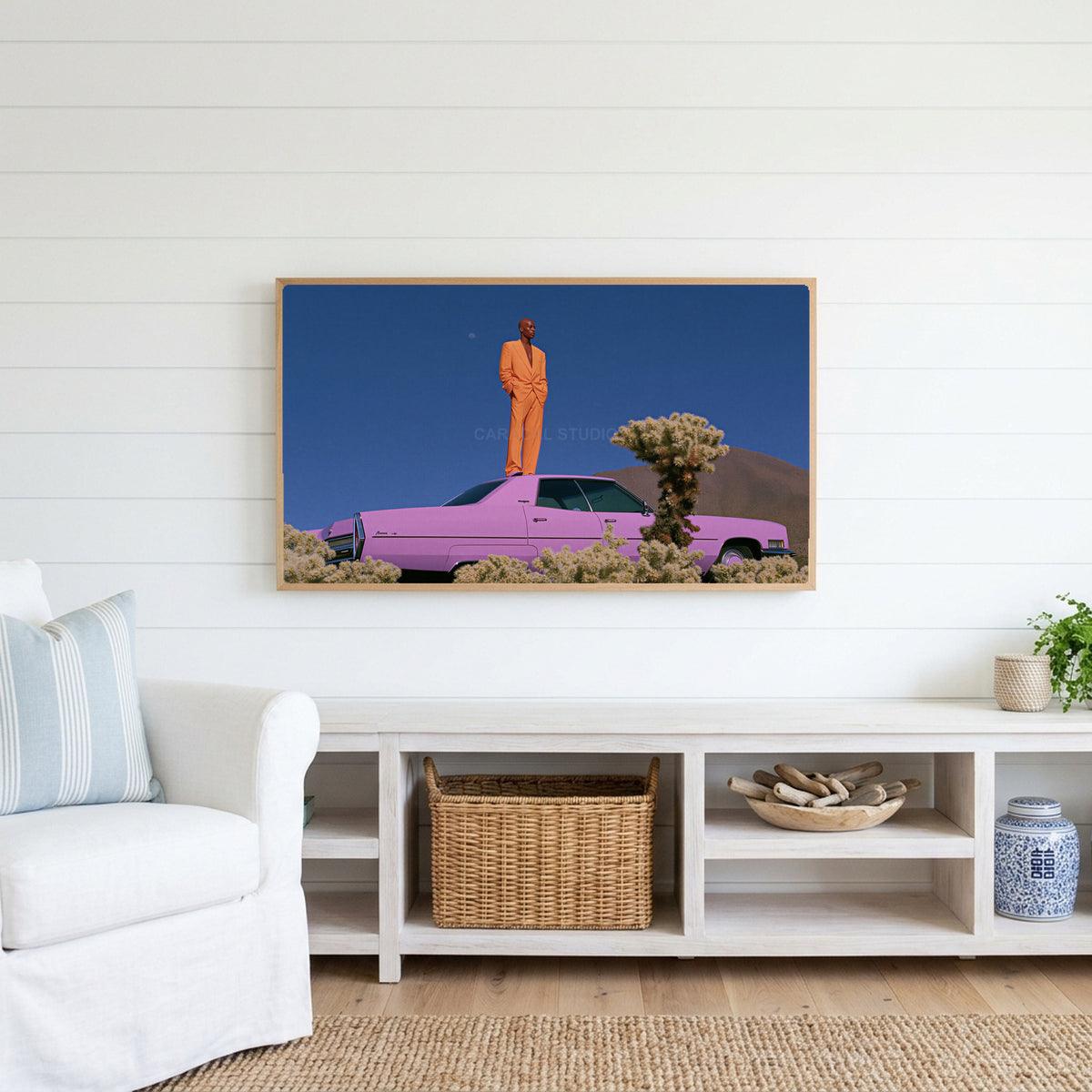 Pink car in the desert Frame TV art above a white console with a rattan basket in a coastal living room