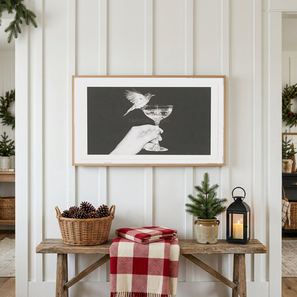 Bird and champagne glass Frame TV art above a rustic bench with pine cones and a red check blanket on a white plank wall