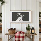 Bird and champagne glass Frame TV art above a rustic bench with pine cones and a red check blanket on a white plank wall
