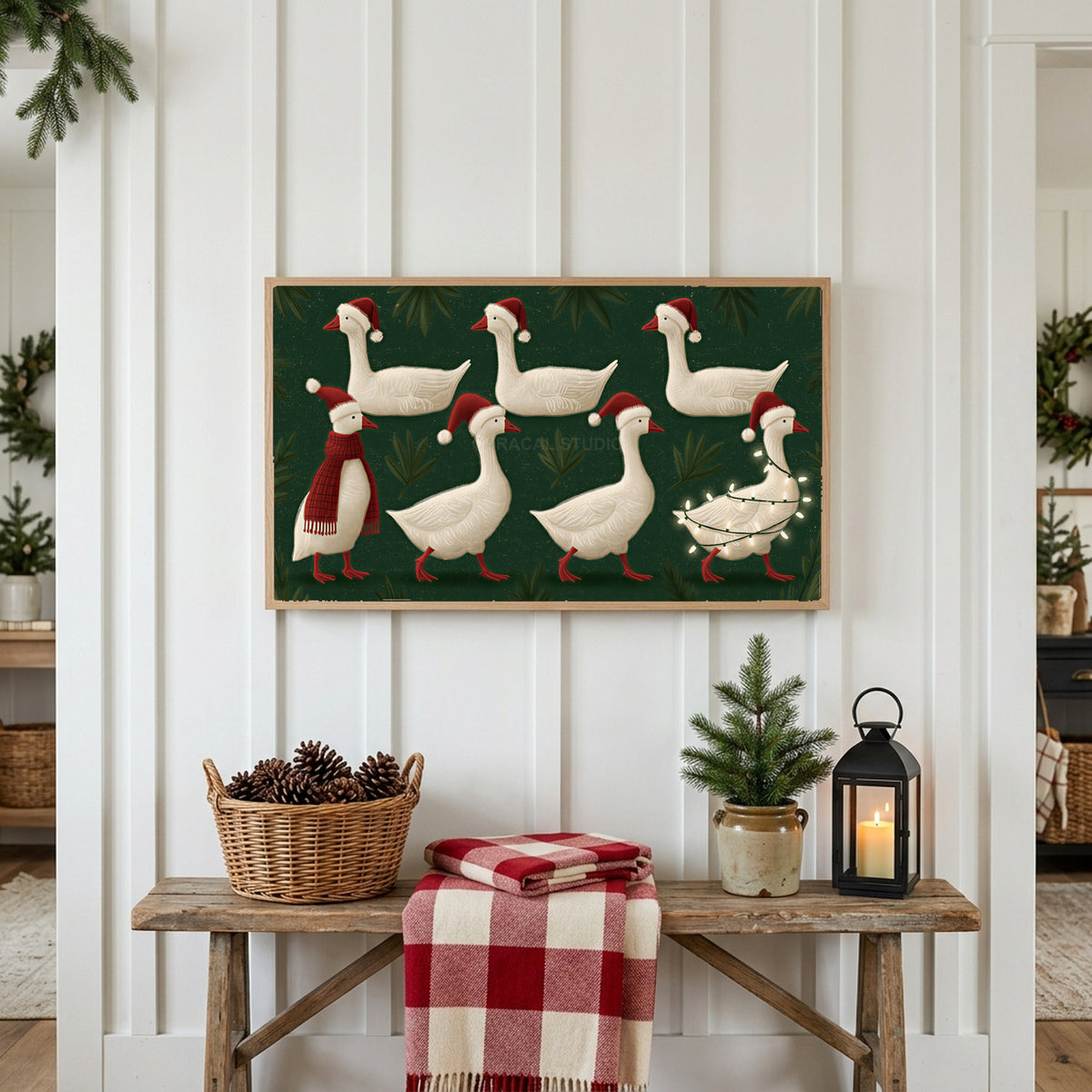 Geese in Santa hats Frame TV art above a rustic bench with pine cones and a red check blanket on a white plank wall