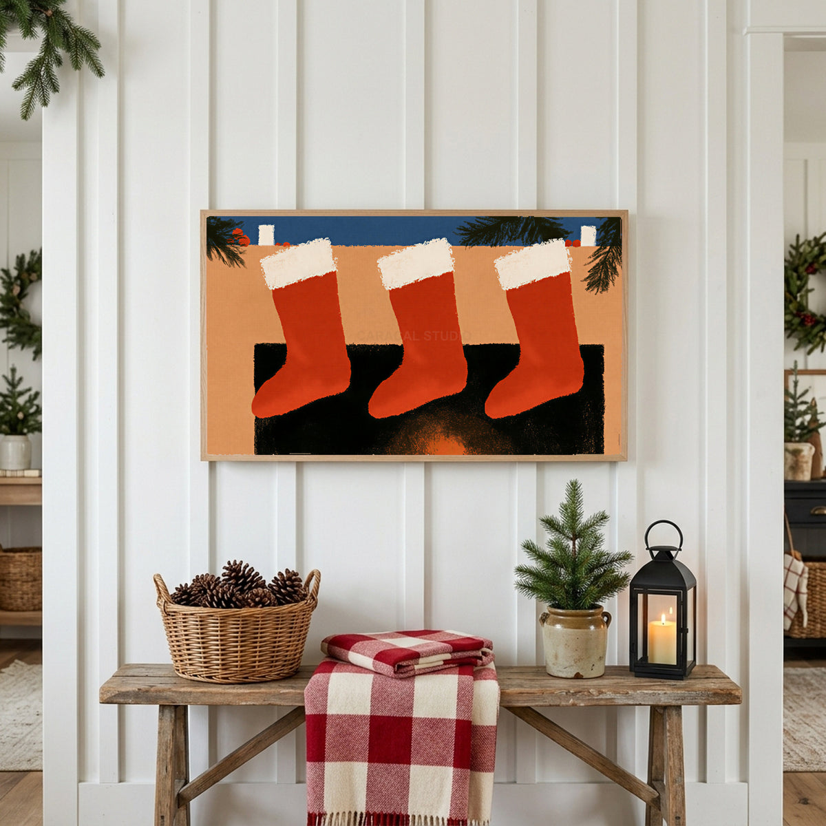 Stockings on the mantel Frame TV art above a rustic bench with pine cones and a red check blanket on a white plank wall