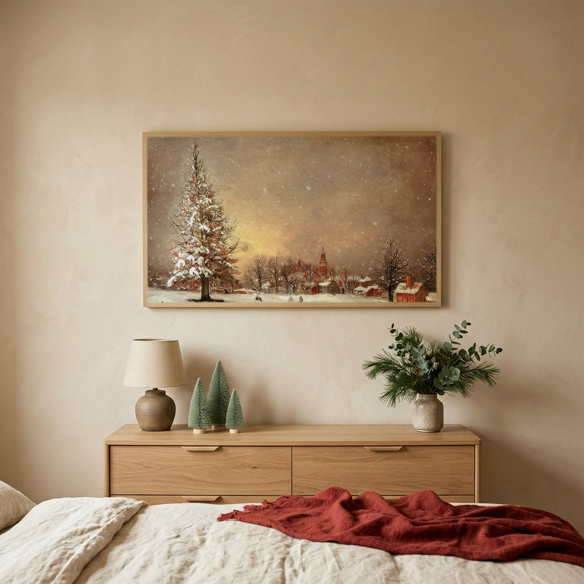 Snowy tree and village Christmas TV art above an oak dresser with small bottle-brush trees in a calm bedroom