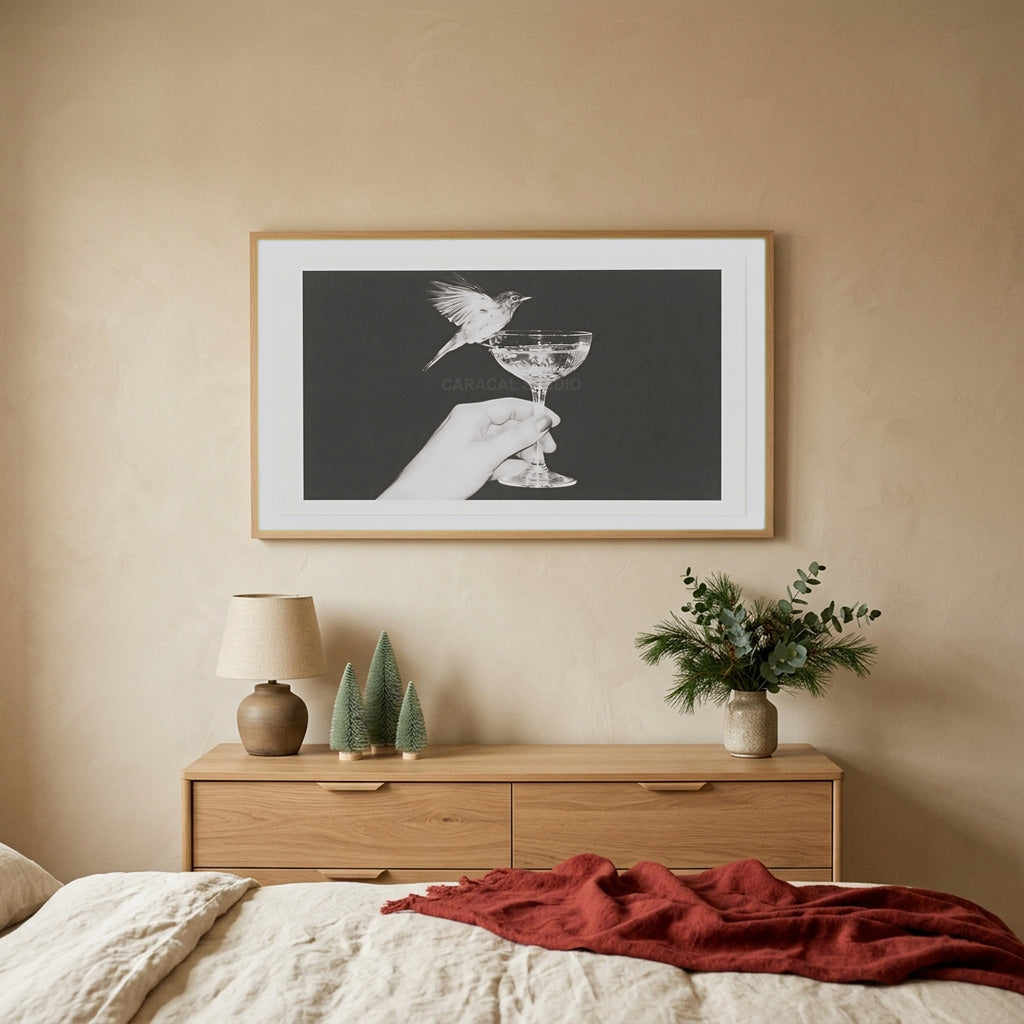 Bird and champagne glass TV art above an oak dresser with small bottle-brush trees in a calm bedroom