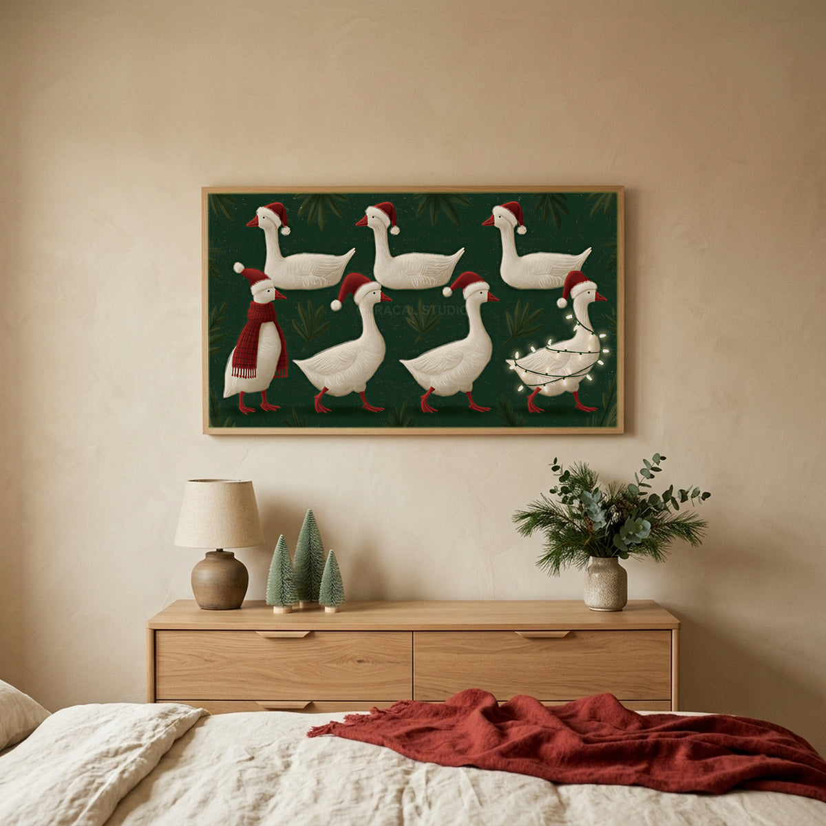 Geese in Santa hats TV art above an oak dresser with small bottle-brush trees in a calm bedroom