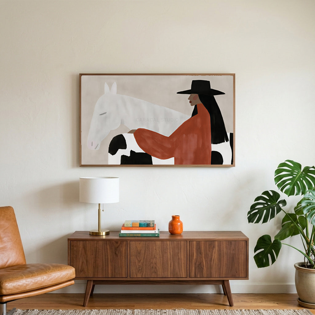 Cowgirl and her horse art on a TV above a walnut credenza with a brass lamp and a monstera plant